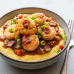 A close-up 45-degree angle shot of a bowl of creamy southern shrimp and grits, garnished with bacon and green onions.