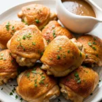 A platter of juicy slow cooker chicken thighs with golden crispy skin, garnished with fresh parsley.